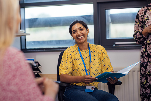 An over-the-shoulder shot of a teacher smiling in a meeting, wearing smart-casual clothing. The teachers are sitting in an office within a secondary school in Gateshead, England.