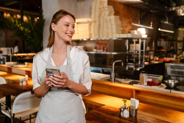 istock Young blonde woman wearing apron using cellphone while working in cafe 1469940939