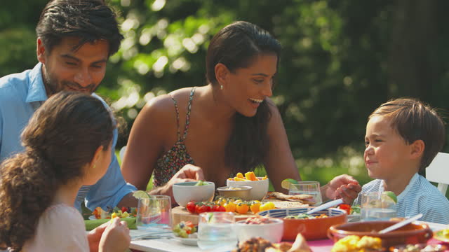 Family Eating Outdoor Meal In Summer Garden At Home Together