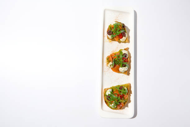 istock Aesthetic composition with salmon bruschetta on white backgroundover white wall. Italian bruschetta with salmon, avocado, cheese and olives on fine dining in summer. Elegant menu concept. 1469942679