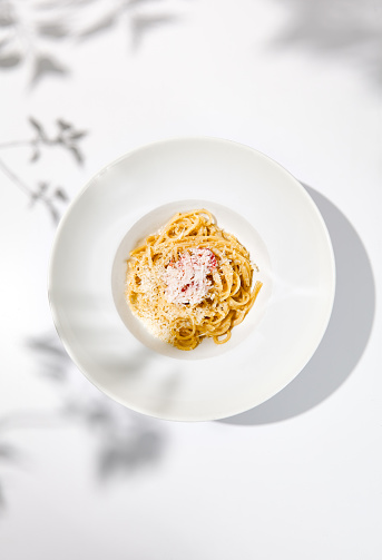 Spaghetti with crab meat and cheese on white table with shadows. Seafood pasta with spaghetti and crab in summer italian menu. Italian pasta with parmigiano cheese and crab meat