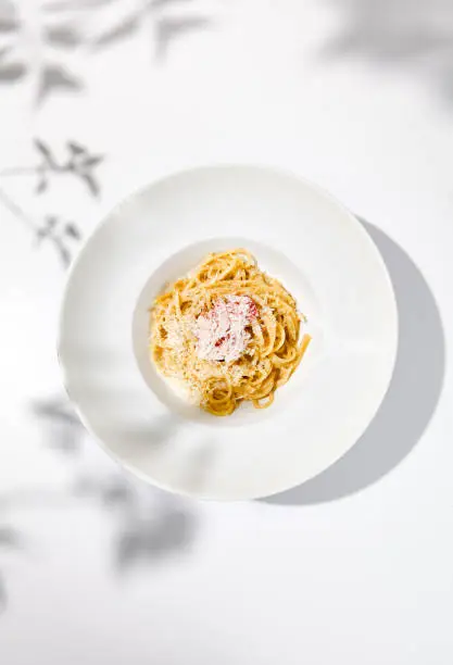 Photo of Spaghetti with crab meat and cheese on white table with shadows. Seafood pasta with spaghetti and crab in summer italian menu Italian pasta with parmigiano cheese and crab meat