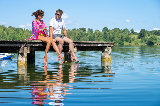 Mature woman talking with mature man while sitting on pier at lake.