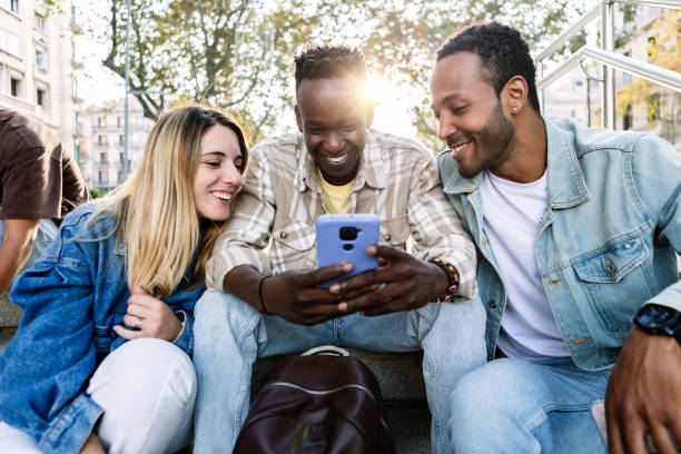 istock Group of multi-ethnic young friends using mobile phone sitting together outdoor 1469944131