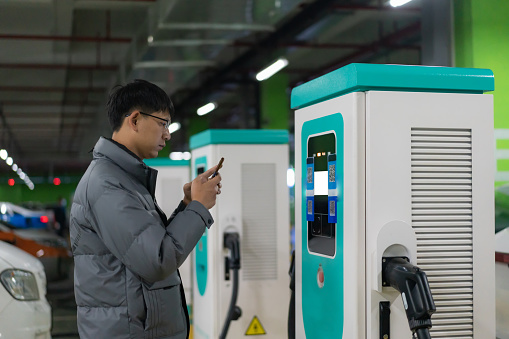 Electric car charging station, Asian man use mobile phone scan code to pay for charging, sustainable living concept