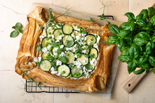 Zucchini and cheese phyllo dough tart with green peas, micro greens and basil. Zucchini and feta pizza, filo puff pastry. Savoury vegetable vegetarian baking. stock photo