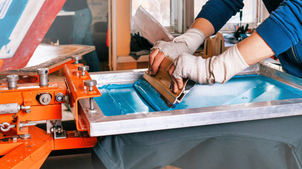 sérigraphie. mains masculines avec une raclette. sérigraphie production photo sélective à mise au point. impression d’images sur des vêtements par sérigraphie dans un studio de design - silk screen photos photos et images de collection