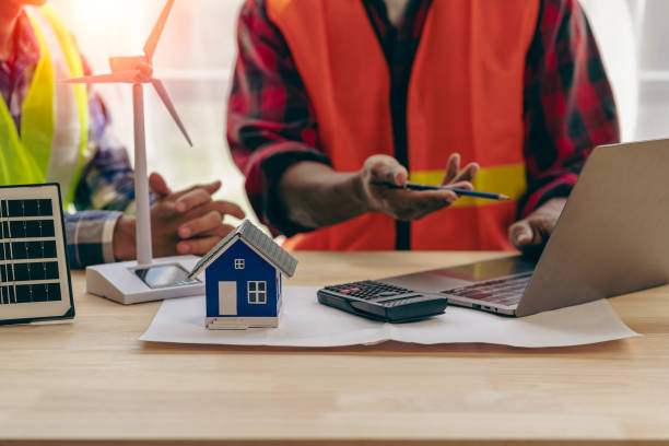 istock Construction team starts new project plans behind yellow helmets on table in office to discuss renewable energy construction projects with wind turbines and solar cells and houses on table. 1469948226