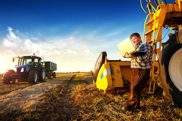 istock A farmer leaning against a combine harvester in the field uses a computer 1469950374