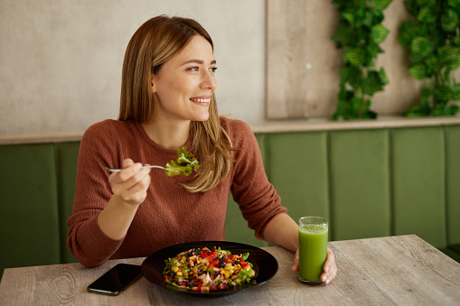 Mid adult woman enjoys eating salad and drinking smoothie in salad bar