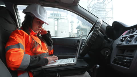 Woman engineer working from car at power plant.