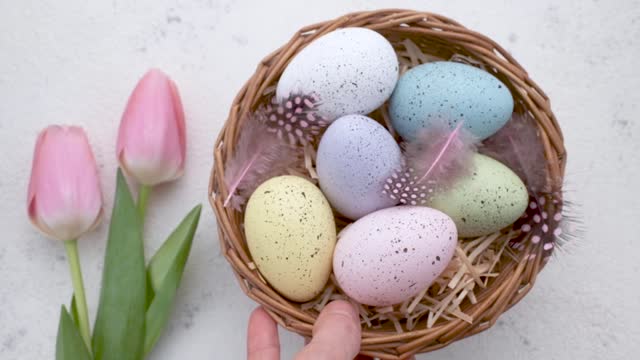 A woman's hand puts a basket with painted Easter eggs on the table.