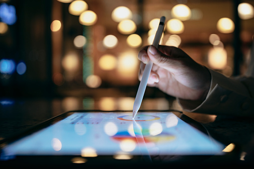 Una persona de negocios está trabajando en una cafetería por la noche, usando una tableta y un lápiz óptico para buscar índices de gráficos y usarlos para proyectos de trabajo. photo