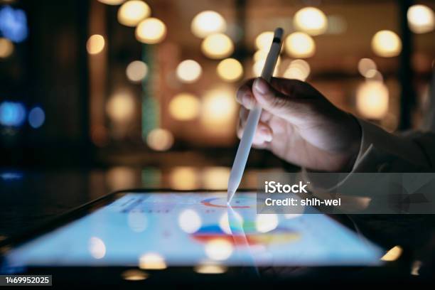 A Business Person Is Working In A Cafe At Night Using A Tablet Device And A Stylus To Look Up Chart Indexes And Using Them For Work Projects Stock Photo - Download Image Now