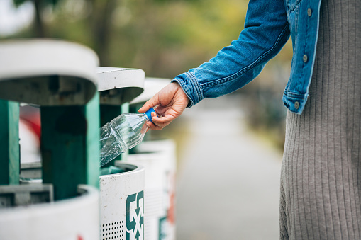 The woman puts a PET bottle into the recycling bin, giving the recyclable waste a chance to be reused and showing her environmental awareness and appreciation for the Earth.