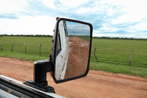 Off road vehicle driving on dirt track passing through landscape reflecting in wing mirror in Los Llanos, Venezuela.