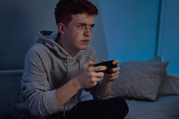 Caucasian teenage boy playing on game controller at night stock photo