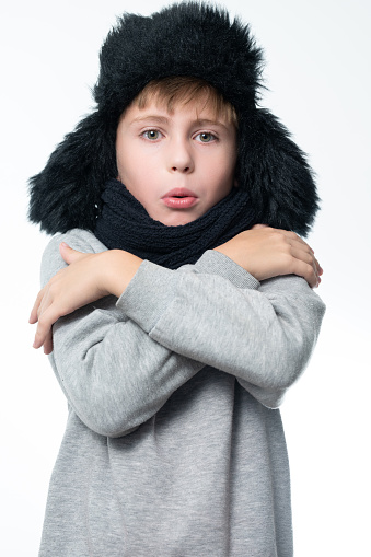 Portrait of a boy on a white background in a hat with earflaps and a scarf, the boy warms himself with his hands from the cold.