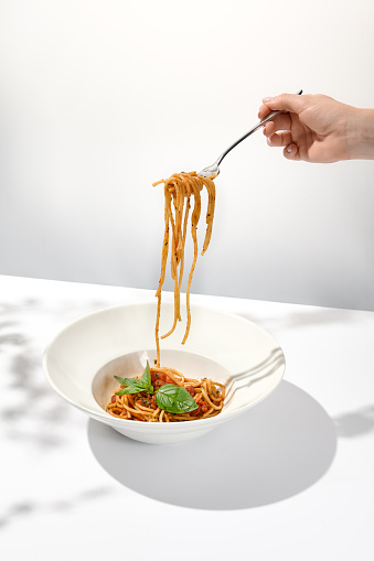 Woman eat italian pasta with tomato and basil. Female hand holding fork with spaghetti over dish. Eating pasta. Person eat italian food. Stretching pasta with woman young hand