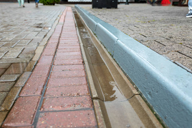istock Rainwater runoff during rain. Concrete gutter for rainwater drainage between the sidewalk and the roadway. Selective focus 1469958652