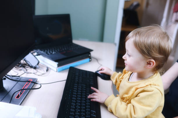 istock Cute 2 year old girl busily working at a home computer 1469958944
