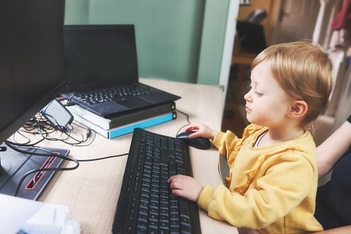 Cute 2 year old girl busily working at a home computer
