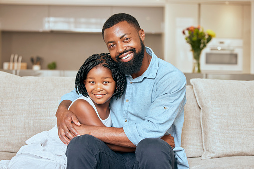 Hug, happy and portrait of a girl with her father on the living room sofa to relax together in a house. Family, love and African dad hugging his child with care and a smile on the couch in their home