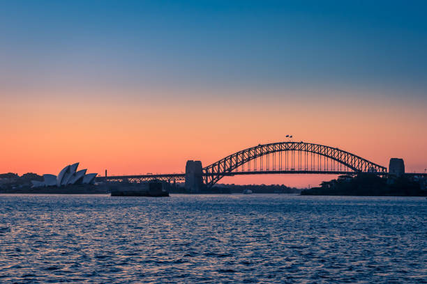 sydney harbor bridge and opera house during sunset seen from the sea, new south wales, australia - international landmark sydney harbor australia new south wales imagens e fotografias de stock