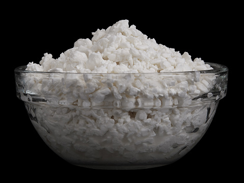 Cottage cheese in glass bowl isolated on black background. Side view of Dairy protein curds