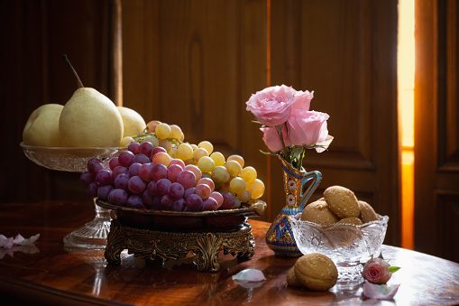 still life with plates full of fruits and flowers in vase on wooden background