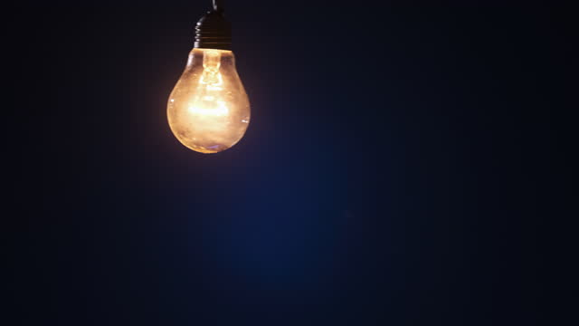 Incandescent Lamp on Wire Sways and Lights Up with Flickers on Dark Background