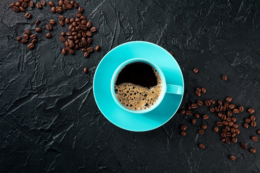 Coffee cup, shot from the top on a black slate background with coffee beans and copy space, espresso drink in a vibrant teal mug