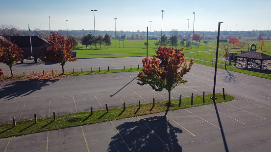 Empty parking lot with colorful fall foliage outside community recreational center with playground and grassy fields in Rochester, New York, USA. Aerial view bright autumn leaves quite parking space