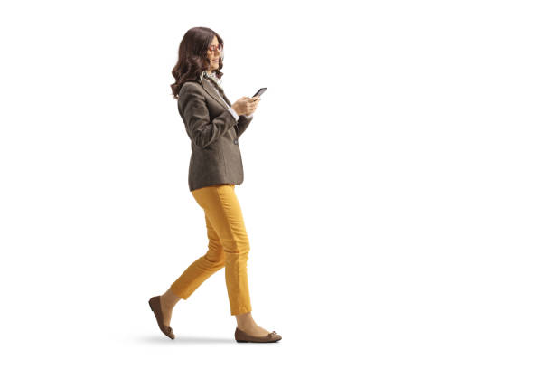 Immagine di profilo a figura intera di una giovane donna in abiti formali che cammina e usa uno smartphone - foto stock