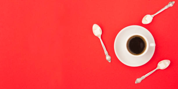 Black coffee in the white cup and spoons with sugar on the red background. Top view. Copy space.