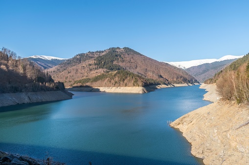 A scenic landscape of a lake surrounded by mountains and trees under the clear blue sky