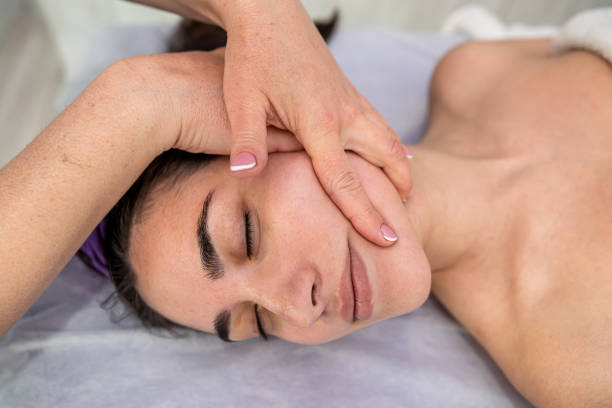istock masseuse hands doing relax massaging female face in spa salon 1469974475