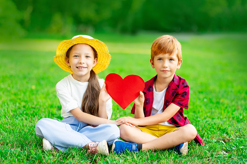 a girl and a boy hold a red heart in their hands on a green lawn in summer, the concept of Valentine's day