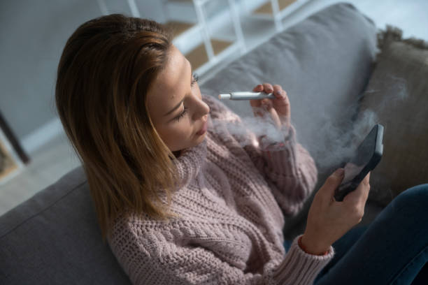 istock Girl relaxes at home with phone and e-cigarette. Vaping. 1469978246