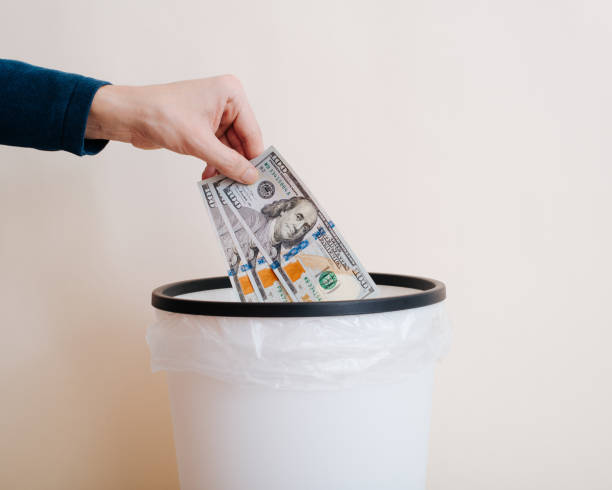 istock Close-up hand throws money, one hundred dollar bills into trash can 1469978464