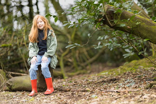 Redhead aged 8 resting on a log in woodland.