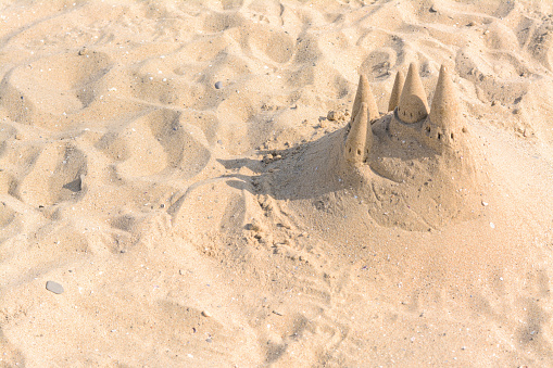 Stock photo showing sandy beach with a sandcastle made with a bucket with a mold shape, in the distant background a boat with punt for tourist cruises is seen, ready for a tour gide to show people around the area