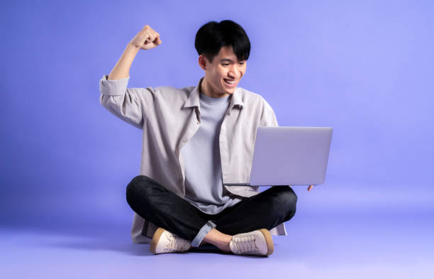 istock full body image of young asian man using laptop on purple background 1469982011