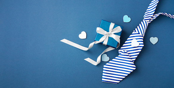 Gift box with white ribbon bow and tie on blue background, happy fathers day concept, top view