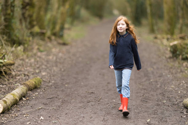 Little redheaded girl striding along a woodland path.