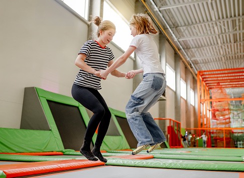 Two girls sisters in trampoline park jumping and having fun together. Happy teenagerand preteen child friends enjoying amusement activities