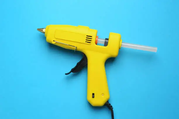 Yellow glue gun with stick on light blue background, top view