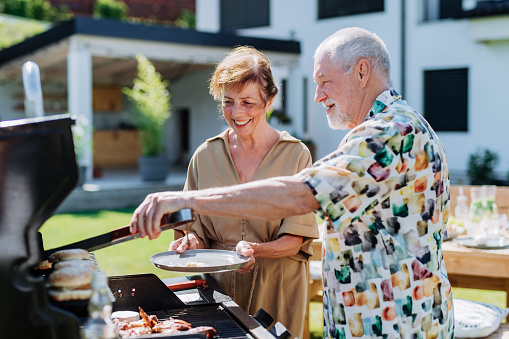 Senior man grilled outdoor at garden, giving his wife fresh hamburger.