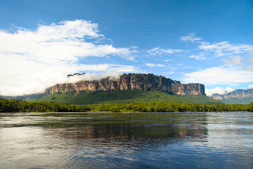 Scenic view of clouds covering Auyan tepui mountain and Rio Churun River in foreground at Canaima National Park, Bolivar State, Venezuela.