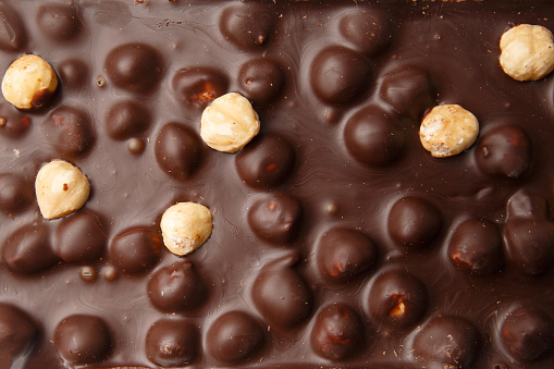 Background of dark chocolate and hazelnuts. Black handmade chocolate with nuts top view macro shot.